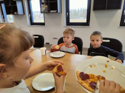 Dwóch chłopców i dziewczynka siedzą przy stole i jedzą pizze.