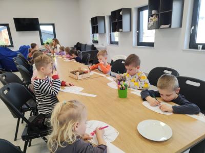 Dzieci siedzą przy stole i kolorują czapki kucharskie