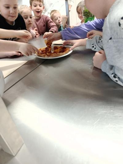 Przedszkolaki częstują się upieczoną pizzą, która leży przed nimi na talerzu