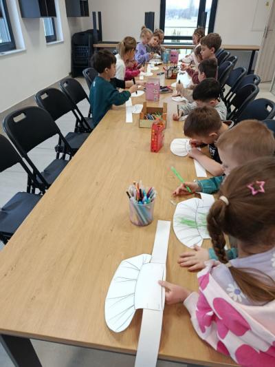 Przedszkolaki siedzą przy stole i ozdabiają mazakami.