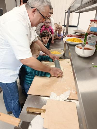 W kuchni dzieci obserwują sposób wałkowania ciasta przez kucharza i jedno dziecko.