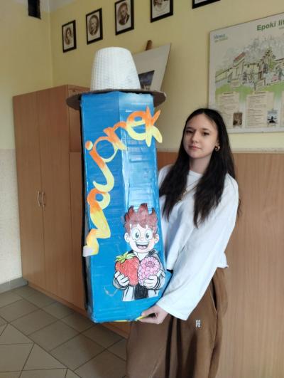 Zwycięzca konkursu na najciekawszy zamiennik plecaka - dziewczynka trzyma zrobioną z kartonu dużą butelkę Wojanka