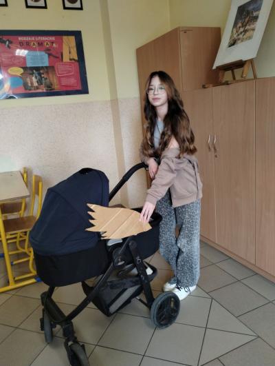 Uczennica klasy 6b z wózkiem dziecięcym z przypiętymi do niego skrzydłami z tektury.