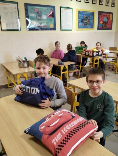 Na zdjęciu dwaj uczniowie klasy 4a, jeden przyniósł poduszkę zamiast plecaka, drugi torbę na zakupy. W tle inni uczniowie klasy.