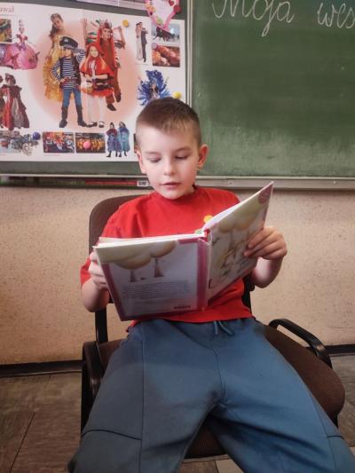 Chłopiec trzyma w rękach ksiażkę i ją czyta.