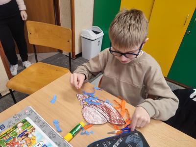 Uczniowie siedzą przy stoliku i rysują, wycinają