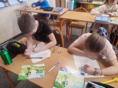 Uczniowie siedzą przy stoliku i rysują, wycinają