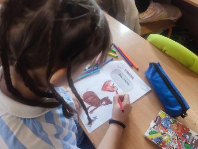 Uczniowie siedzą przy stoliku i rysują, wycinają