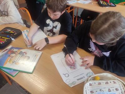 Uczniowie siedzą przy stoliku i rysują, wycinają
