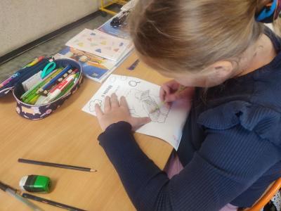 Uczniowie siedzą przy stoliku i rysują, wycinają