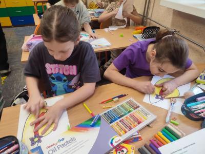 Uczniowie siedzą przy stoliku i rysują, wycinają