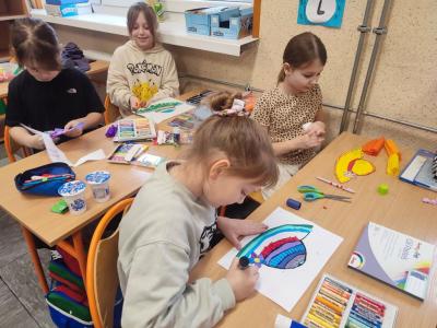 Uczniowie siedzą przy stoliku i rysują, wycinają