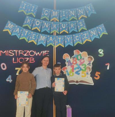 Nauczyciel pozuje do zdjęcia z dwójką dzieci biorących udział w konkursie