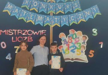 Nauczyciel pozuje do zdjęcia z dwójką dzieci biorących udział w konkursie.