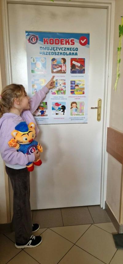 Dziewczynka wskazuje ręką na plakat z projektu Dwujęzyczny przedszkolak