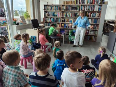 Dzieci z grupy Biedronki w Bilitece w Libuszy siedzą przed p. bibliotekarką. W tle regały z książkami