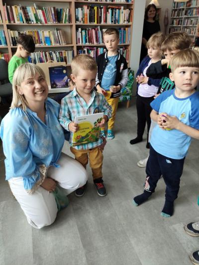 Chłopczyk dostaje prezent z okazji urodzin od pani bibliotekarki. W tle  stoją dzieci