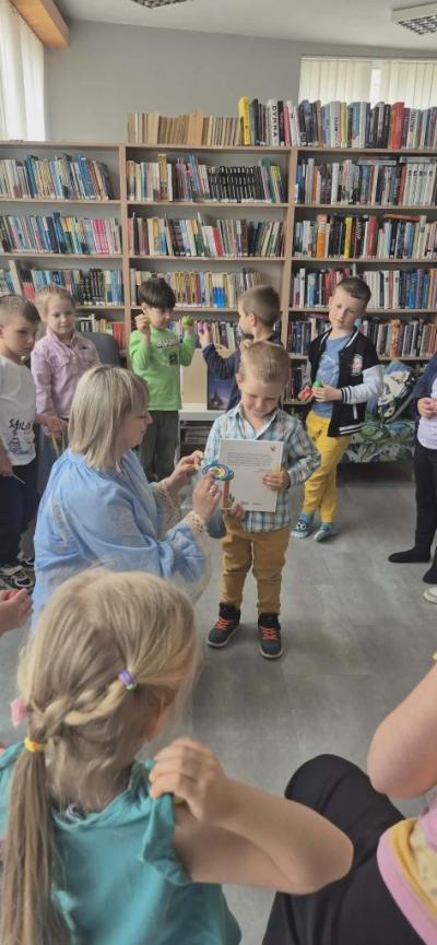 Chłopczyk dostaje pamiątkowy medal od pani bobliotekarki. w tle stoją dzieci