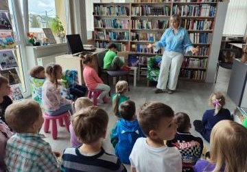Dzieci z grupy Biedronki w Bilitece w Libuszy siedzą przed p. bibliotekarką. W tle regały z książkami.