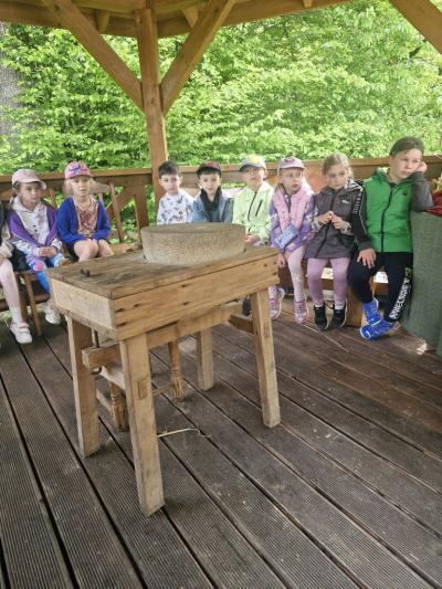 Dzieci siedzą przy żarnie i słuchają opowieści gospodyni