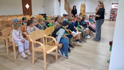 Dzieci siedzą na krzesełkach i odpowiadają na pytania pani przewodnik.