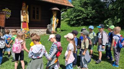 Przedszkolaki idące parami za panią przewodnik w słoneczny dzień podczas spaceru edukacyjnego.