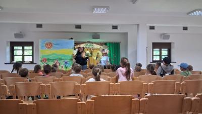 Zdjęcie przedstawia teatrzyk kukiełkowy wewnątrz budynku.  Panie prowadzą spektakl dla dzieci trzymając w rękach kukiełki.