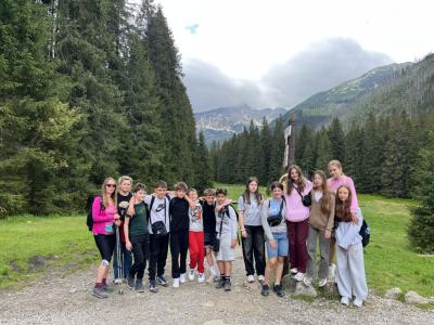 uczniowie stoją z 2 nauczycielkami w pobliżu schroniska w Dolinie Kościeliskiej, w tle Tatry