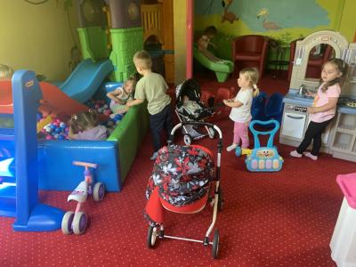 Dzieci wesoło bawią się w sali zabaw wózeczkami dla lalek,  w basenie z kulkami, w kąciku do gotowania