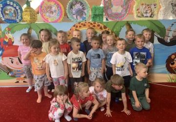 Grupa dzieci pozuje do zdjęcia przed kolorową ścianą z piniatami w sali zabaw.
