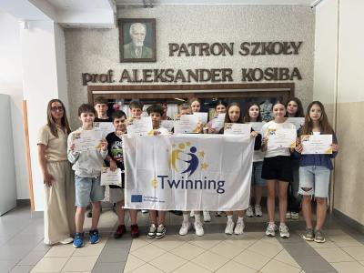 zdjęcie uczniów klasy 6b wraz z nauczycielką , uczniowie trzymają dyplomy i flagę etwinning