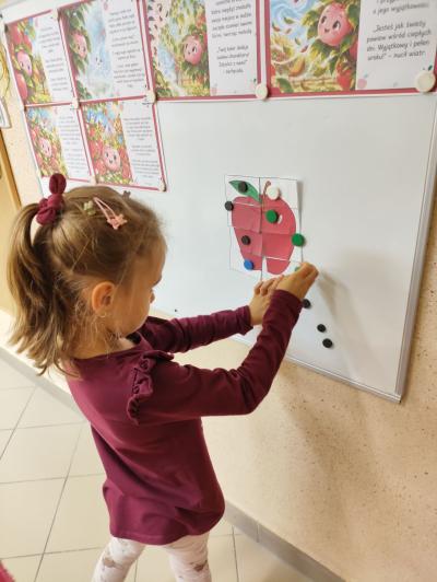 Dziewczynka układa puzzle na kształt czerwonego jabłka