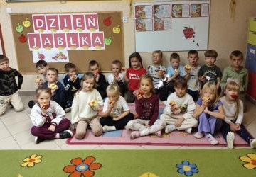 Dzieci jedzą jabłka na tle tablicy z okazji Dnia Jabłka.