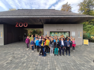 Zdjęcie grupowe przed krakowskim zoo. Obie klasy czwarte pozują do zdjęcia. W tle kasa biletowa