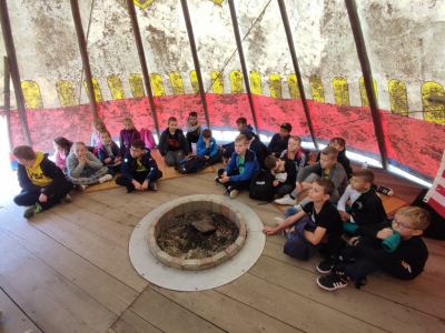 Wizyta w Globalnych Wioskach Świata. Dzieci siedza w środku tipi - uczestniczą w warsztatach edukacyjnych. Na środku palenisko. W środku panuje półmrok