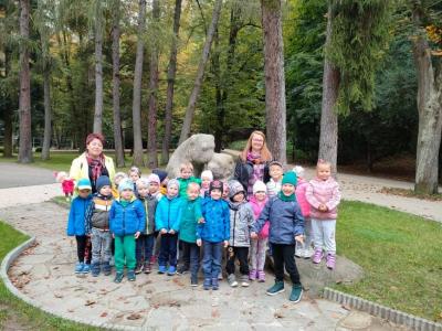 Zdjęcie grupy Leśne Duszki w Parku Miejskim  w Gorlicach. W tle pomnik – dwa przytulone misie