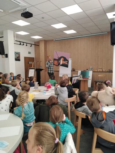 Pisarz stoi przed dziećmi i pokazuje im dużą ilustrację, przedstawiającą lisa.