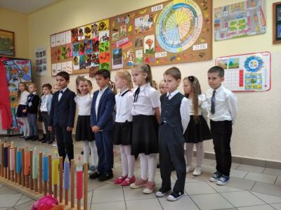 Dzieci stoją w dwóch rzędach. Ci z przodu mówią wierszyki. Z lewej strony widać jesienną dekorację przewieszoną flagą biało- czerwoną.