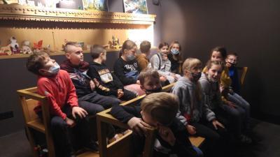 Grupa uczniów siedzi na drewnianych ławeczkach, w formie wozu i ogląda krośnieńskie legendy.