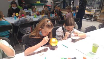 Dzieci uczestniczą w warsztatach malowania bombek choinkowych. Siedza przy stołach i ozdabiają szklane kule.