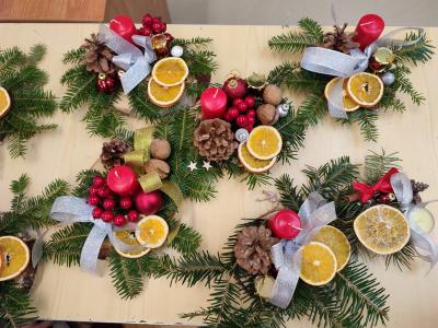 Na stole stoją stroiki świąteczne ozdobione bąbkami, pamarańczami, świecami, szyszkami.