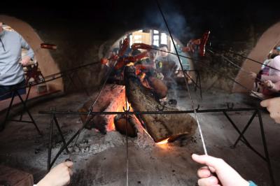 Dzieci pieką kiełbaski nad ogniem. Na środku pali się ognisku w dyzym murowanym piecu.