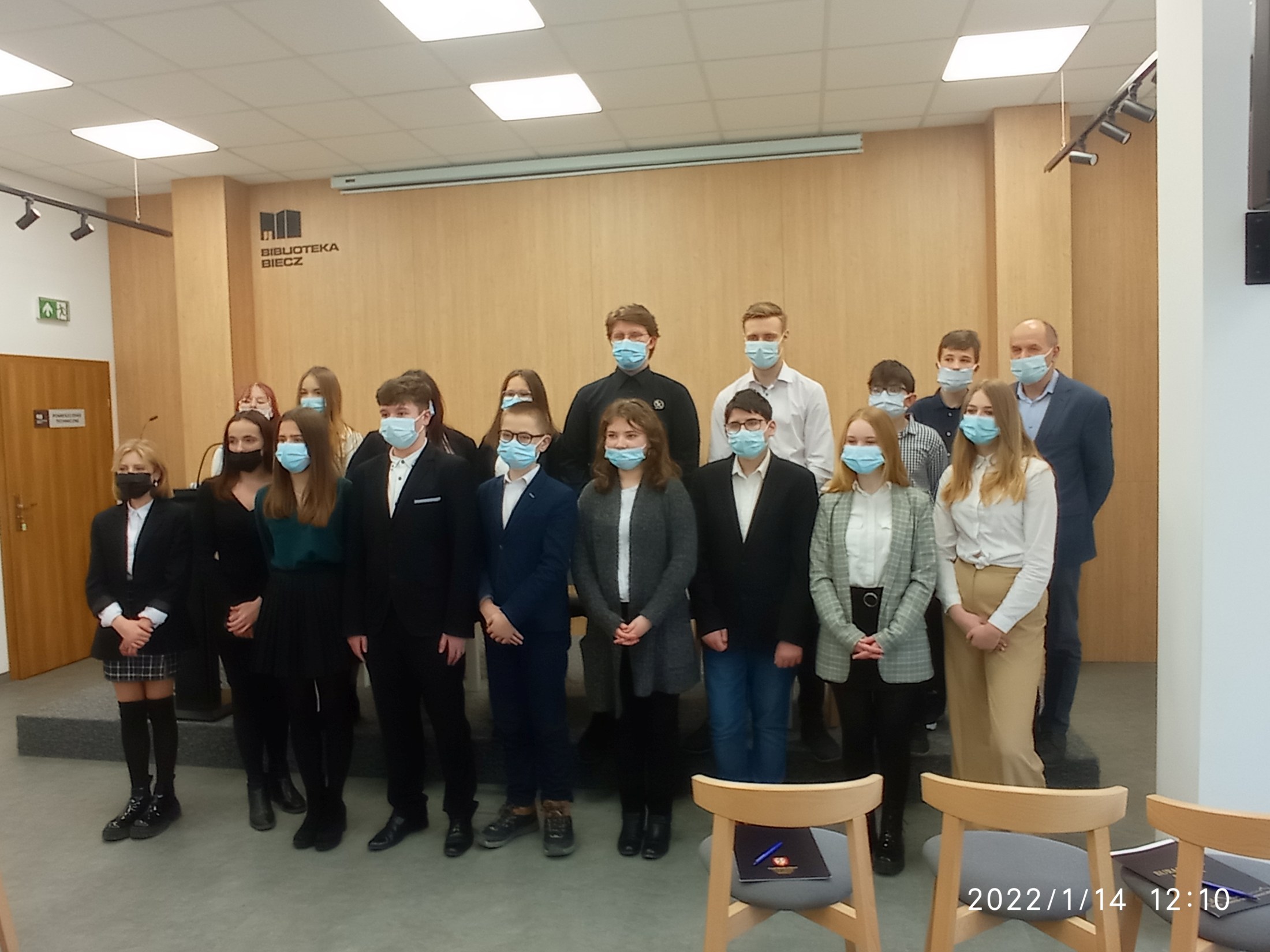 Na zdjęciu stoi grupa uczniów, są to przedstawiciele szkół podstawowych i ponadpodstawowych z gminy Biecz wraz z opiekunem Młodzieżowej Rady Miejskiej, panem Jerzym Mikosem. Członkowie MRM mają zakryte maseczką ochronną usta i nos.