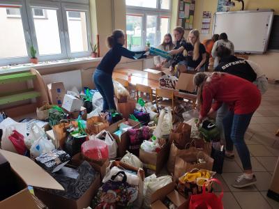Zbiórka darów dla uchodźców - torby z darami, pudełka z żywnością, młodzież szkoły, która sortuje dary i układa do paczek.