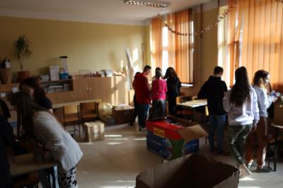 Zbiórka darów dla uchodźców - torby z darami, pudełka z żywnością, młodzież szkoły, która sortuje dary i układa do paczek.