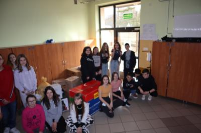 Zbiórka darów dla uchodźców - torby z darami, pudełka z żywnością, młodzież szkoły, pozująca do zdjęcia grupowego.