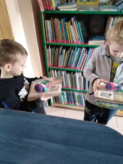 Dwóch chłopców trzyma w rękach zakładki do książek, włóczkowe sówki i książeczkę, które otrzymali na pamiątkę pasowania.