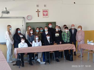 Przedstawiciele MRM wraz z koordynatorem oraz Panią Dyrektor ZSP w Rożnowicach stoją w sali lekcyjnej pod szkolną tablicą. Wszyscy mają zasłonięte usta i nos maseczką ochronną.