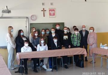 Przedstawiciele MRM wraz z koordynatorem oraz Panią Dyrektor ZSP w Rożnowicach stoją w sali lekcyjnej pod szkolną tablicą. Wszyscy mają zasłonięte usta i nos maseczką ochronną.
