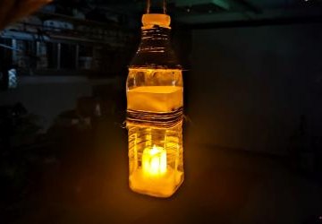 Replika lampy Ignacego Łukasiewicza - w plastikowej butelce świeci znicz na baterie. Butelka ozdobiona sznurkiem jutowym i wstążką.